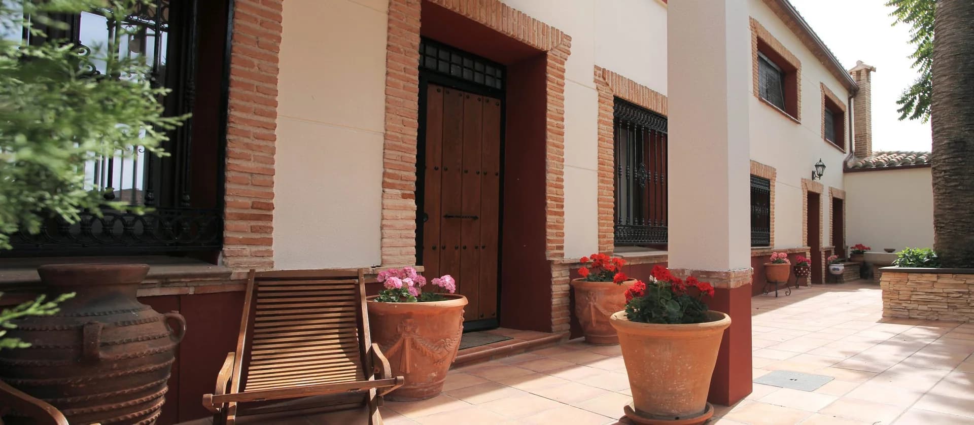 Patio de Tres Ventas con tumbonas de madera, tinajas y geranios